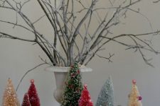 24 a small and colorful holiday arrangement with bright bottle brush trees and mini houses plus branches ina  vintage urn