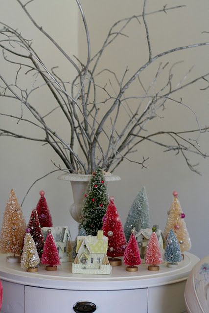 a small and colorful holiday arrangement with bright bottle brush trees and mini houses plus branches ina  vintage urn