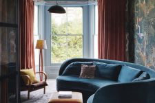 25 a moody and bold living room with a curved blue sofa, orange textiles and moody bird print wallpaper on one wall