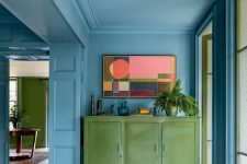 26 a beautiful and chic stone blue space with much natural light, a green credenza, potted plants and a bold artwork