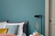 27 a soothing and chic stone blue bedroom with a bed with muted color bedding, a white round nightstand and a black lamp