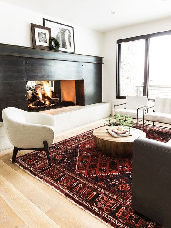 a bold burgundy and red printed rug adds color the monochromatic room and makes the living room bolder and more chic