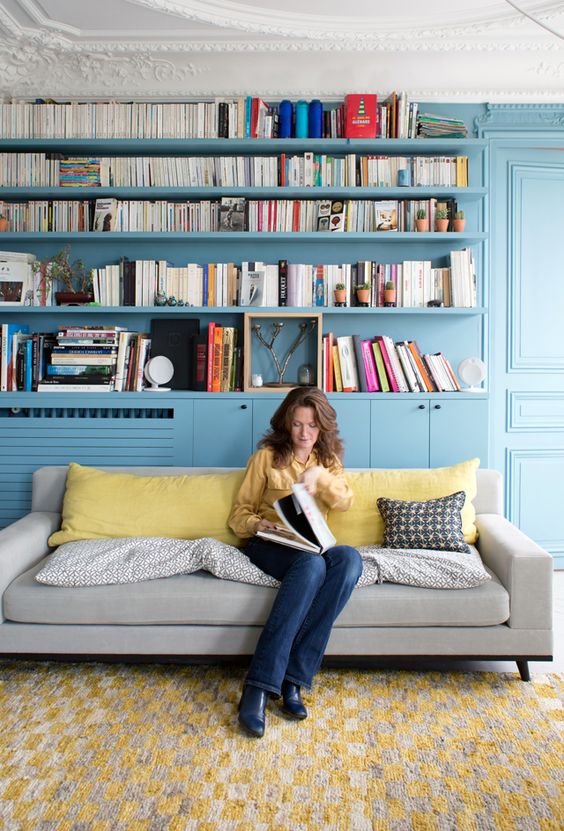 a living room and library done in stone blue - all the walls, shelves and storage units plus yellow accents in the space