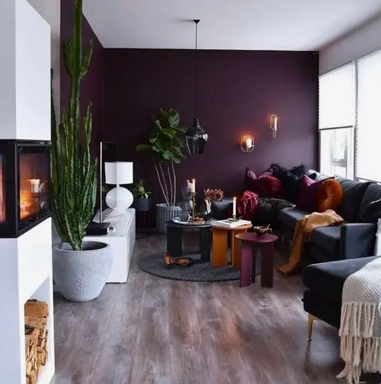 a beautiful contemporary living room with a deep purple accent wall, a black sofa and a chair, colorful coffee tables, potted plants and a fireplace