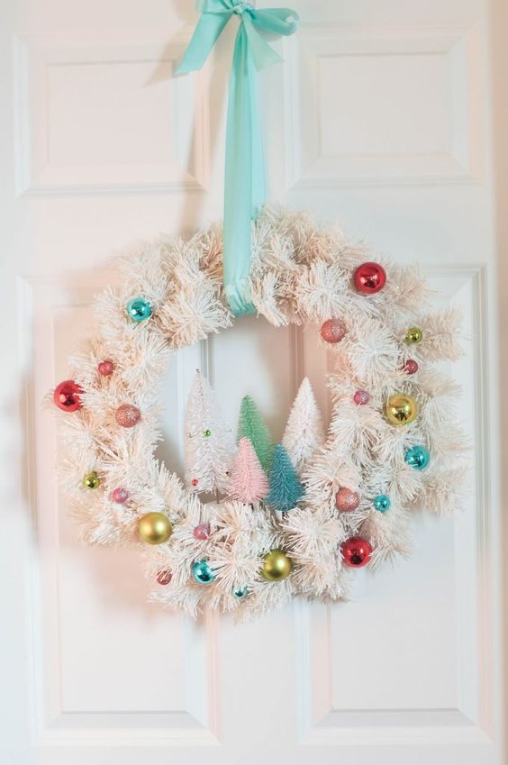 a white evergreen Christmas wreath decorated with colorful ornaments and colorful bottle brush Christmas trees