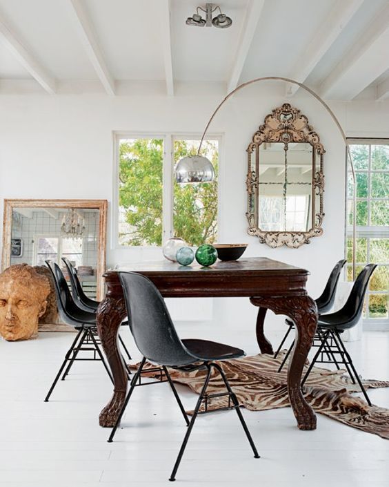 a gorgeous dining room with a vintage dark-stained dining table, modern black chairs and a bold accent rug