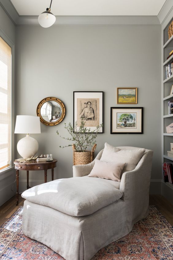 a lovely reading nook in dove grey, with a built-in bookcase, a neutral lounger, a mini gallery wall and a vintage side table