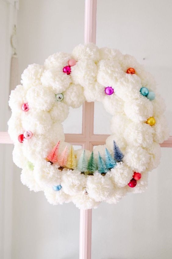 a white pompom Christmas wreat decorated with colorful ornaments and colorful bottle brush Christmas trees