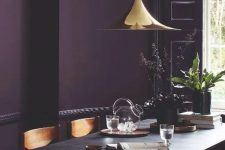 35 a moody dining room with an aubergine accent wall, a black trestle table and wooden chairs, a shiny gilded pendant lamp