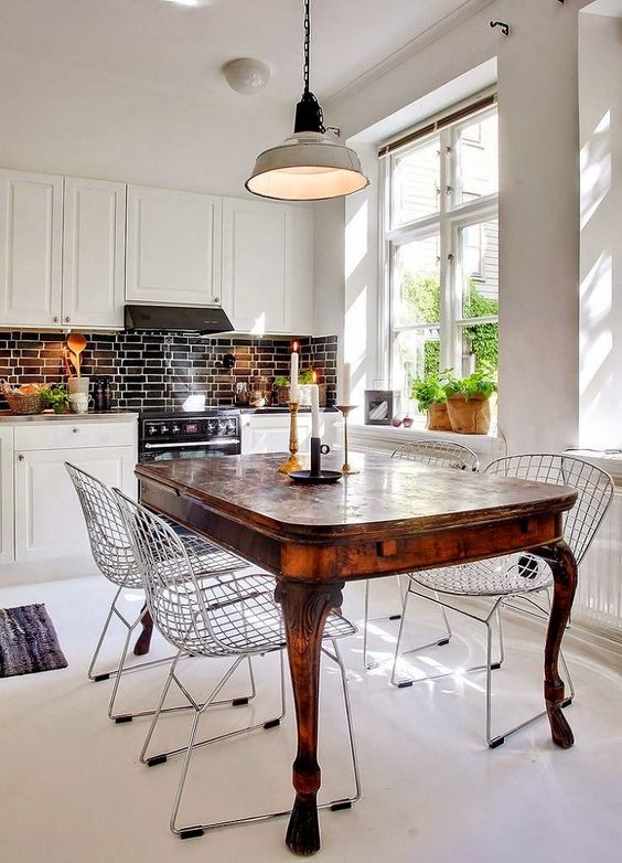 a white eat-in kitchen with a black tile backsplash, a rich-stained dining table and modern wire chairs for a contrast
