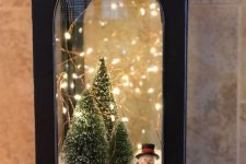 37 a black metal lantern with faux snow, bottle brush Christmas trees, lights and a small snowman is a lovely idea