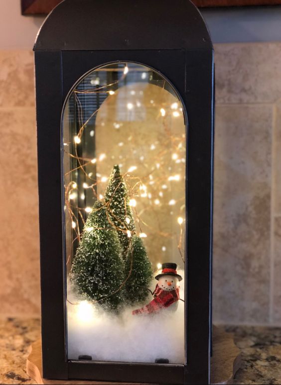 a black metal lantern with faux snow, bottle brush Christmas trees, lights and a small snowman is a lovely idea