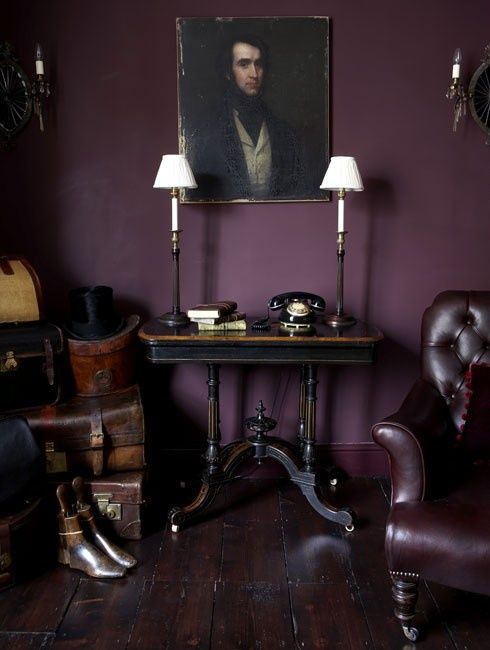 a vintage aubergine space with dark heavy vintage furniture, a pretty artwork, chic lamps and sconces is elegant