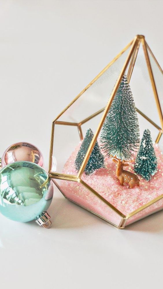 an elegant Christmas terrarium with pink faux snow, green bottle brush trees and a little deer figurine is chic and cute