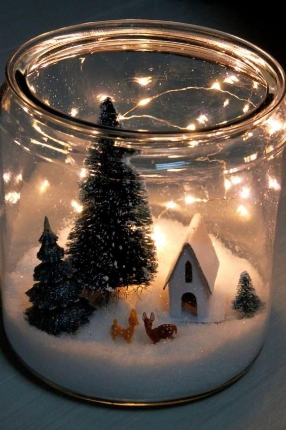 an oversized jar with faux snow, little deer figurines, a house and some bottle brush trees and lights is pure magic