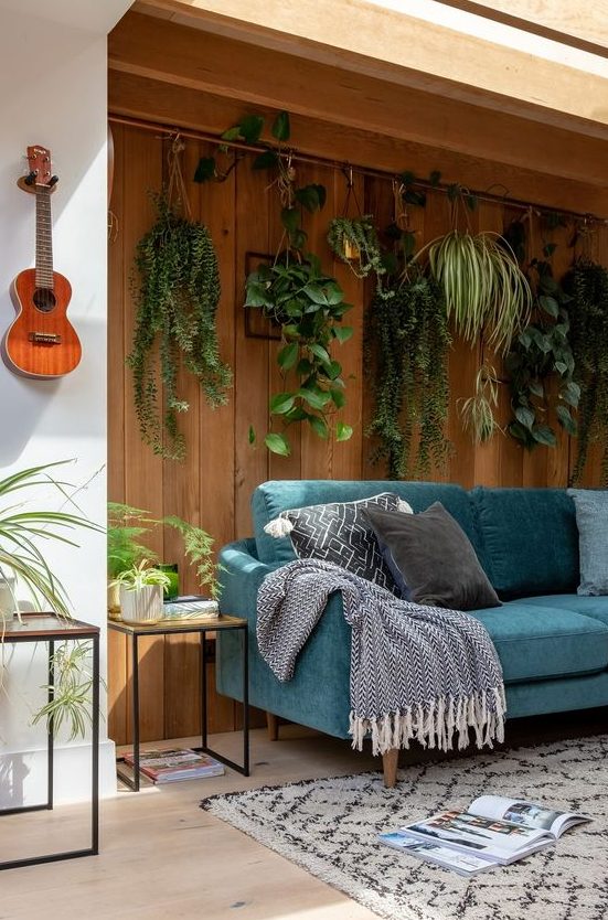 a biophilic living room with potted plants suspended over the sofa to the natural wooden wall