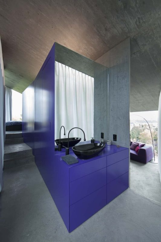 a bathtoom cluster completely hidden with bold periwinkle panels, a black sink, a black faucet and neutral curtains