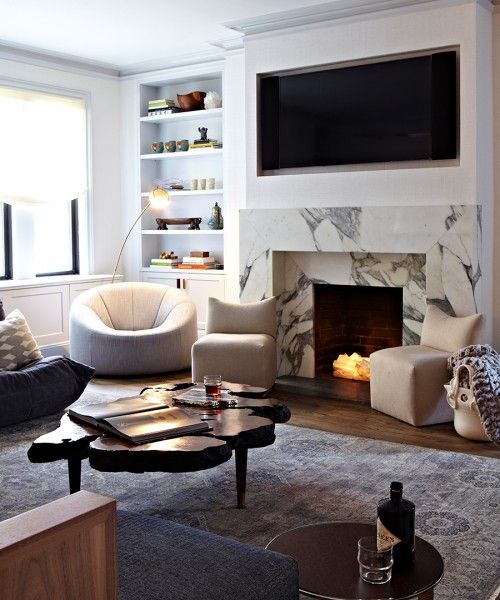 a beautiful and catchy modern living room with a built-in white marble fireplace, a built-in TV, built-in shelves, white and grey furniture and a wood slice table