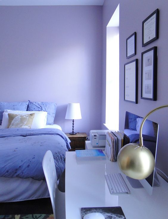 a beautiful periwinkle bedroom with a bed with white and very peri bedding, a sleek white desk and a white chair, a small gallery wall