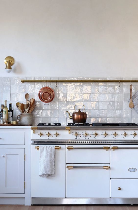 a beautiful vintage white kitchen with gold fixtures and a gorgeous white zellige tile backsplash that adds shine, interest and texture
