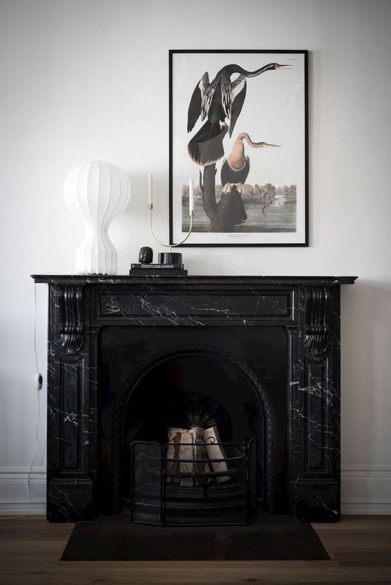 a black marble fireplace and some chic decor on the mantel and a whimsy artwork for a chic and refined space