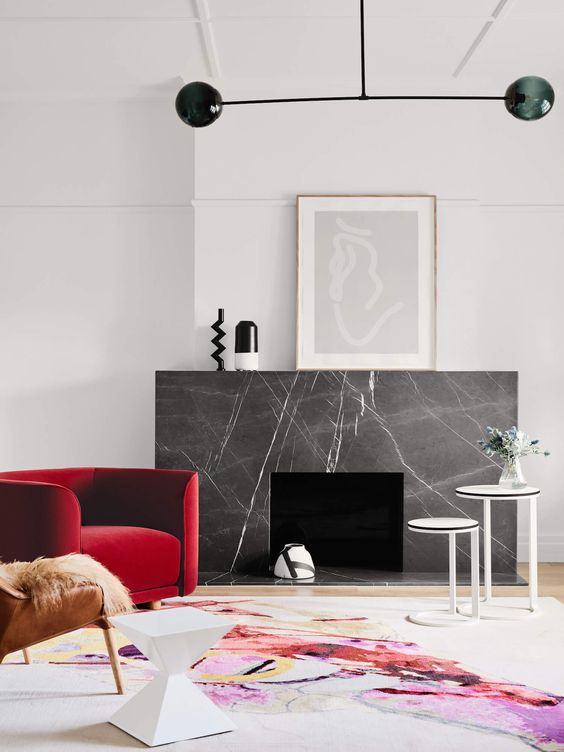 a-bold-modern-space-with-a-fireplace-clad-with-grey-marble-a-red-chair-and-a-leather-one-a-bold-rug-a-black-chandelier-and-some-art.jpg