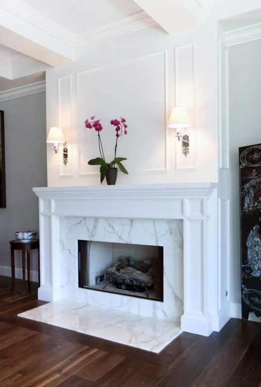 a chic and stylish marble fireplace with some marble on the floor and a vintage white mantel over it is refined