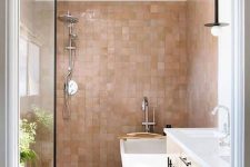 a chic bathroom with white furniture and appliances and lovely pink and tan zellige tiles covering the walls in the bathing space and giving it a soft and warming glow