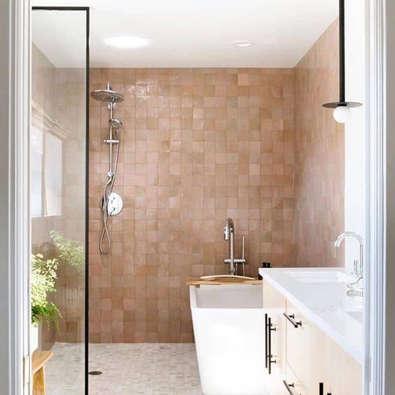 a chic bathroom with white furniture and appliances and lovely pink and tan zellige tiles covering the walls in the bathing space and giving it a soft and warming glow