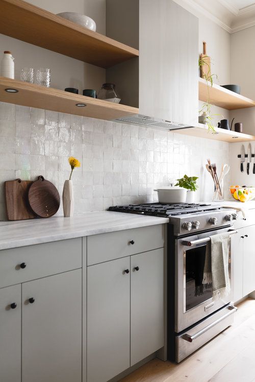 a chic dove grey kitchen with a white zellige tile backsplash, light-stained shelves and white stone countertops is amazing