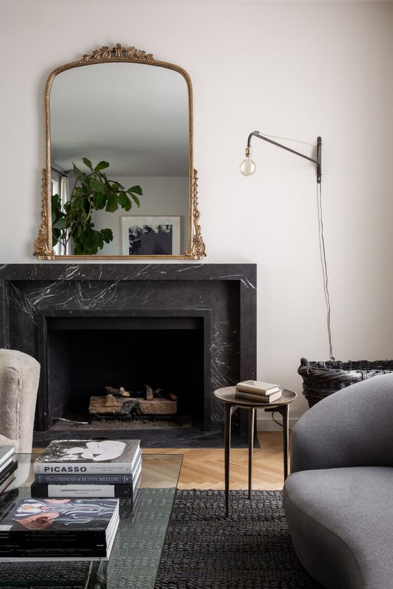 a-chic-space-with-a-black-marble-fireplace-neutral-and-grey-seating-furniture-a-sconce-a-mirror-with-an-adorned-frame-and-greenery.jpg