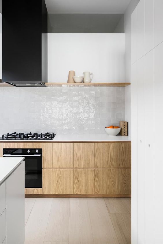 a contemporary kitchen with stained cabinets, white stone countertops, white zellige tiles on the backsplash, a black hood