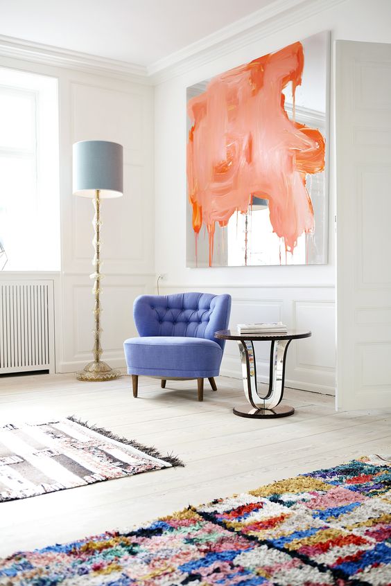 a creamy space with a pretty round periwinkle chair, bright rugs, a mirror with peachy and orange splashes