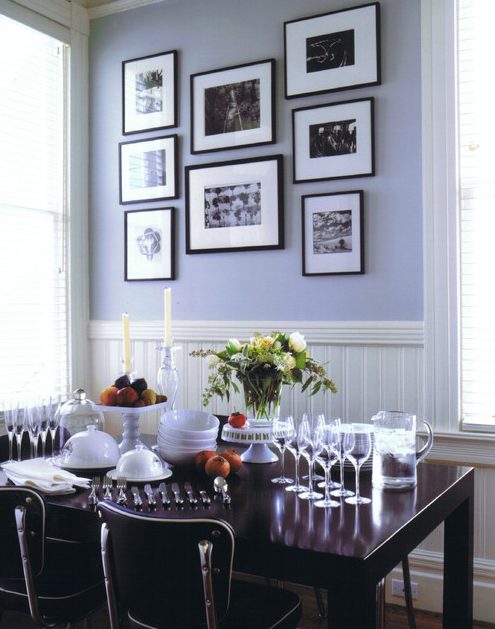 a dining room with periwinkle walls, white wainscoting, a dark-stained table and chairs, a black and white gallery wall