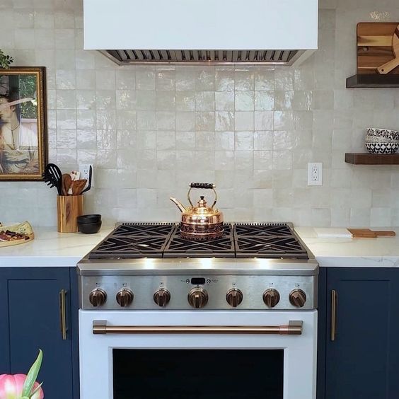 a fantastic navy kitchen with a white cooker and a hood plus fabulous mother of pearl zellige tiles for a soft touch