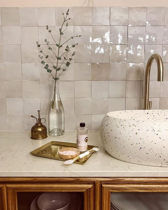 a gorgeous bathroom with a vintage feel, with neutral zellige tiles, a terrazzo sink, a white stone countertop and brass fixtures