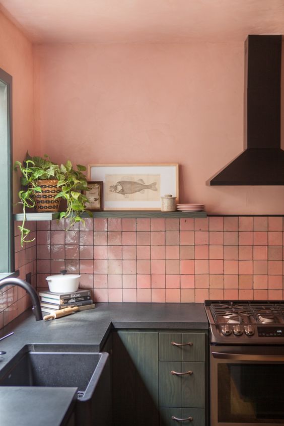 a gorgeous kitchen with pink zellige tiles, green cabinetry, black appliances and fixtures, a shelf with some art and a potted plant