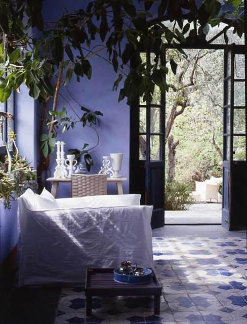 a gorgeous periwinkle sunroom with refined windows and doors, white and stained wood furniture and potted plants and trees