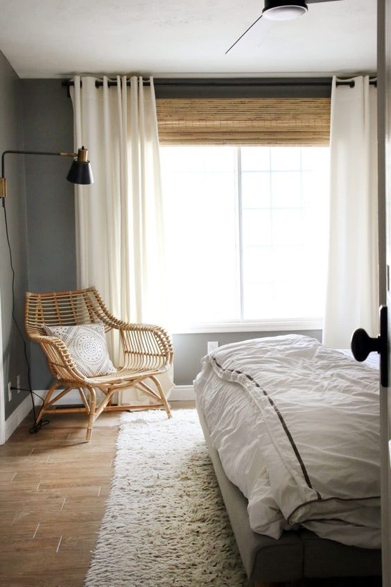 a large woven shade and creamy draperies add coziness and interest to the bedroom, and the shade echoes with the rattan chair