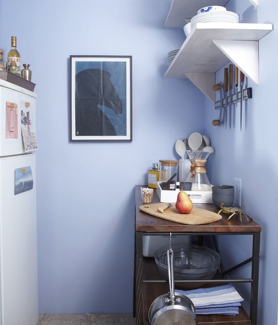 a lovely very peri kitchen with a white fridge, white shelves and a stained kitchen island with an industrial feel plus some art