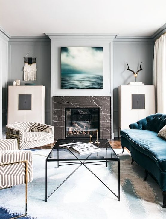 a modern chic living room with a fireplace clad with brown marble, with a glass table and a blue sofa is dreamy