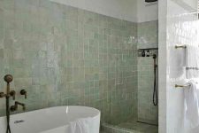 a neutral bathroom with bathing spaces clad with green zellige tiles and the rest of the space done with usual white ones