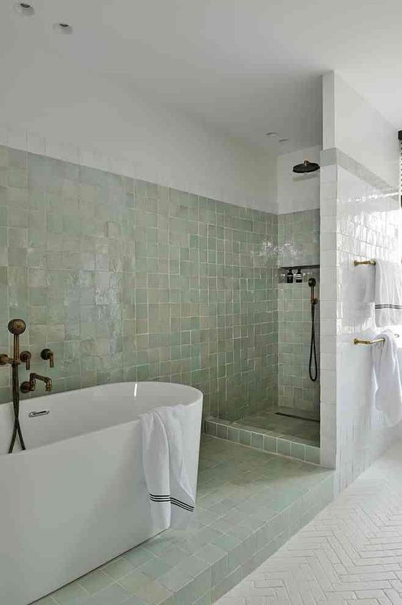 a neutral bathroom with bathing spaces clad with green zellige tiles and the rest of the space done with usual white ones