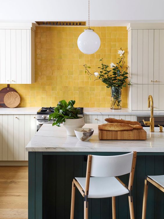 a neutral farmhouse kitchen with planked cabinets, a dark green planked kitchen island and a yellow zellige tile backsplash