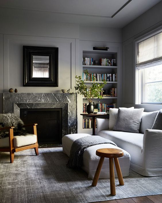 a neutral living room with dove grey walls and built-in shelves, a white sofa and a bench, a fireplace clad with black marble