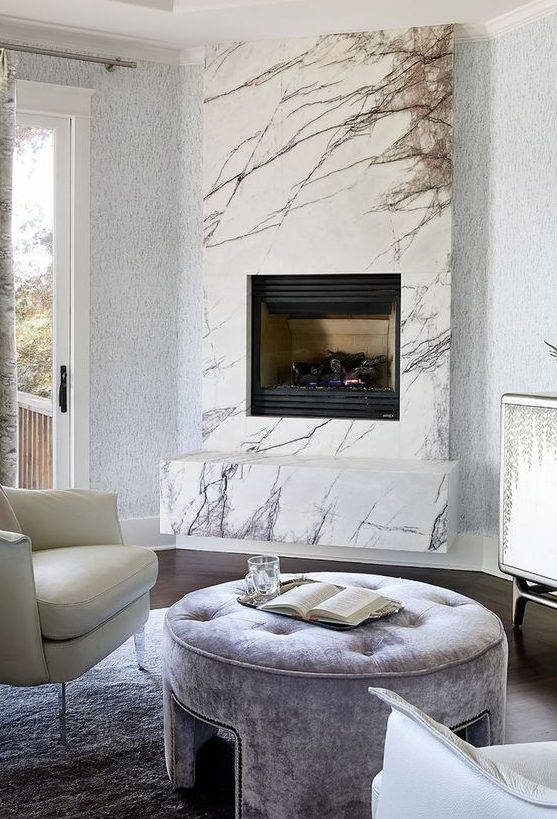 a neutral luxurious living room with a marble clad built-in fireplace and refined leather and velvet furniture
