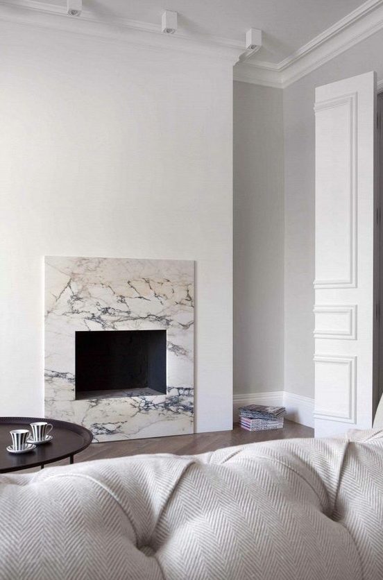 a neutral minimalist living room with a non-working fireplace clad with white marble for a chic and cool touch