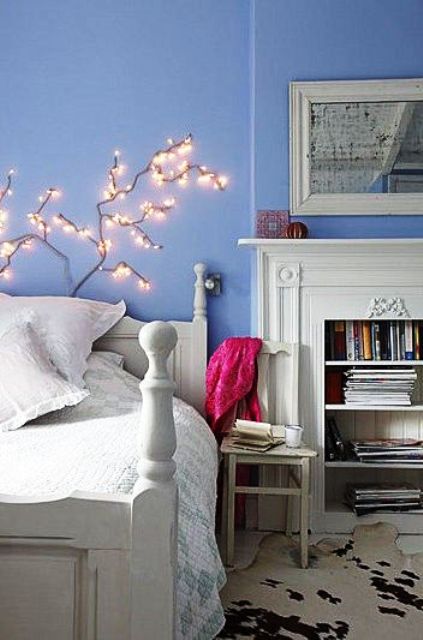 a periwinkle bedroom with a white mantel over a non-working fireplace, a white vintage bed with white bedding, a LED branch over the bed and a vintage mirror