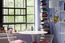 a pretty periwinkle space with a catchy window, a shelving unit, a white tale and wire chairs, a stack of books