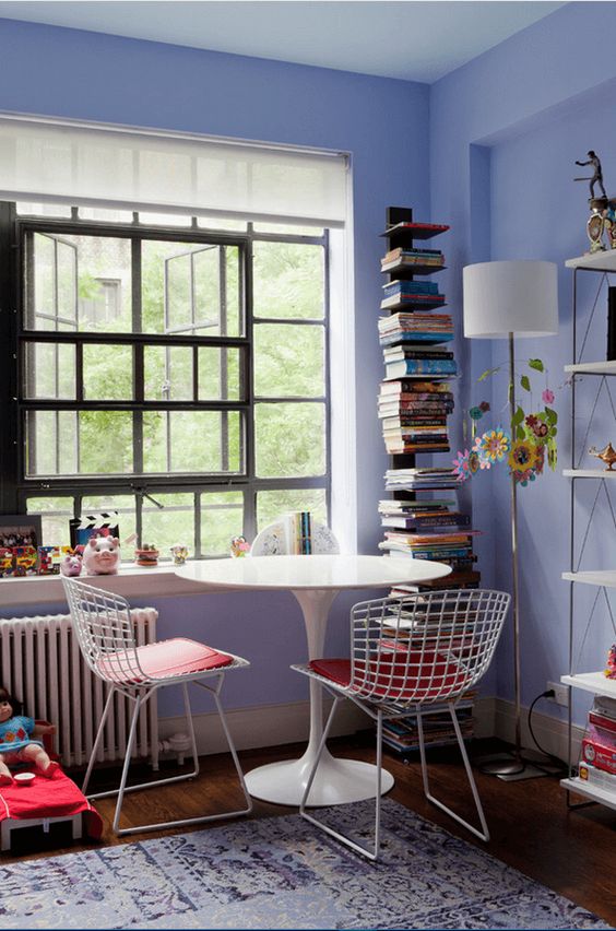 a pretty periwinkle space with a catchy window, a shelving unit, a white tale and wire chairs, a stack of books